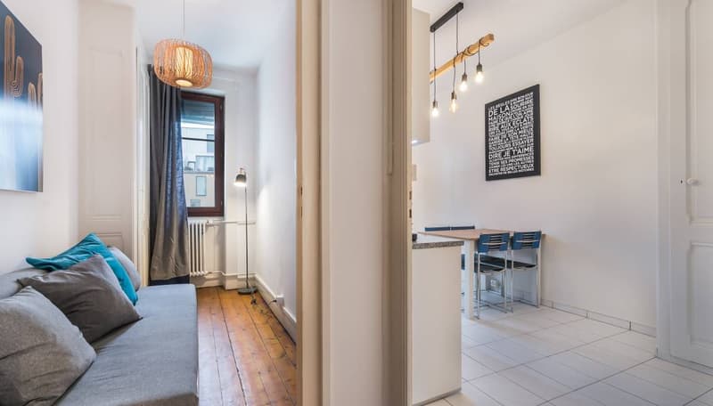 wooden floor, grey couch, pillows, table with blue chairs, lamp, blackboard