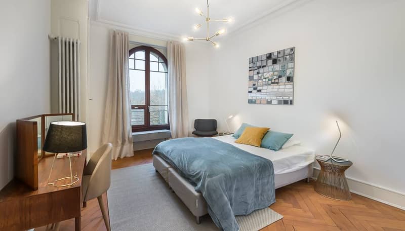 wood floor, arched window, desk, lamp, bed, pillows, radiator, painting, armchair
