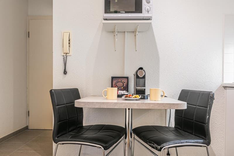 Small dining area with table, two chairs, microwave, telephone, plate with candies, and two coffee mugs