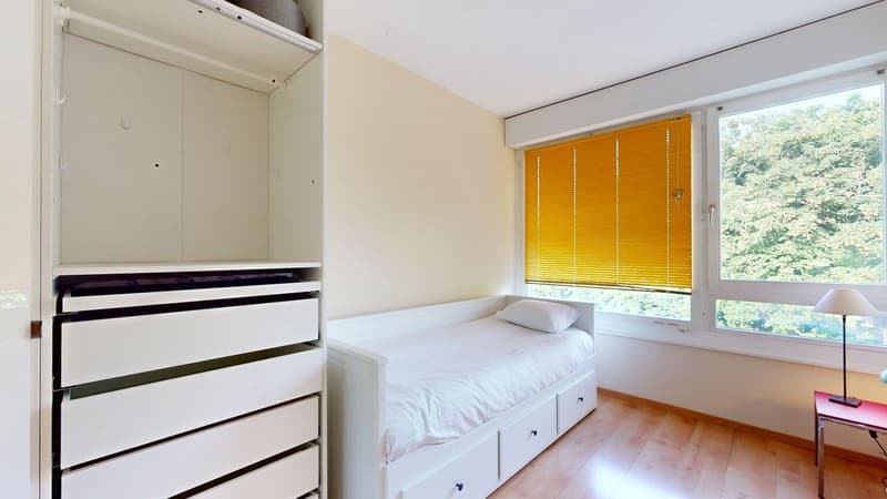 room with bed, white closet with drawers, lamp, yellow blinds, view of trees
