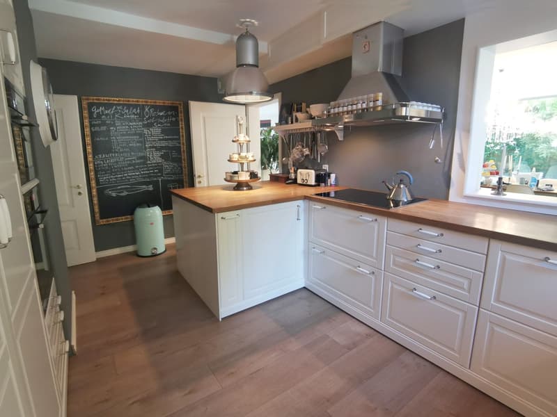 modern kitchen with white cabinets, wooden countertops, island with cooking range, sink, and teapot, open shelving, potted plant, blackboard, ceiling lamp, dishwasher