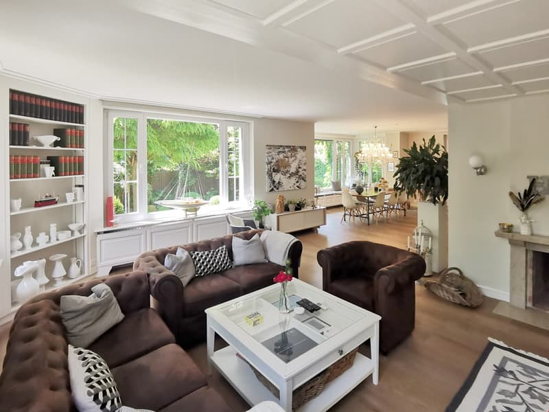 white ceiling, white walls, brown leather sofas, glass table, center table with flowers, fireplace, white cabinets, white shelf with books and cups, large windows