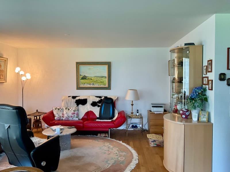 The living room has a red couch, floor lamp, round coffee table, round rug, black leather chair, side table with lamp, and a wooden cabinet with a printer on top.