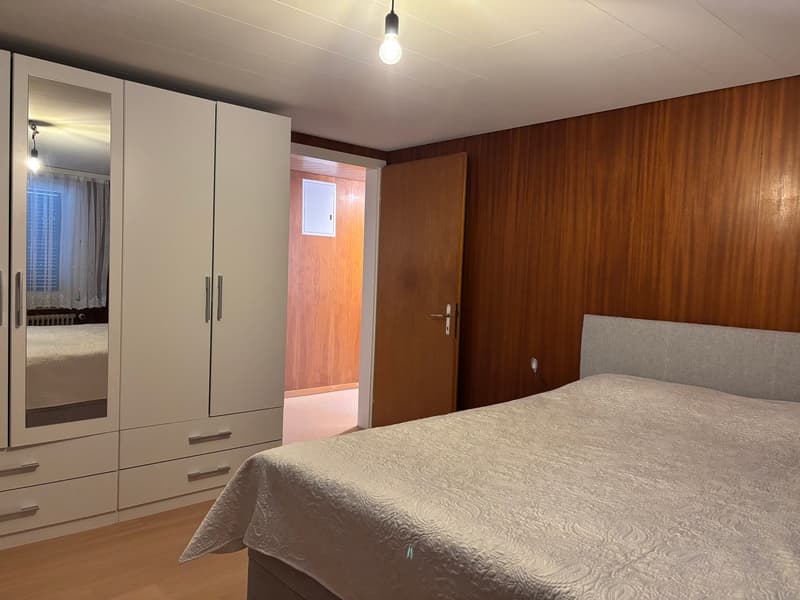 Bedroom with bed, wardrobe, mirror, wooden wall, wooden floor, light bulb
