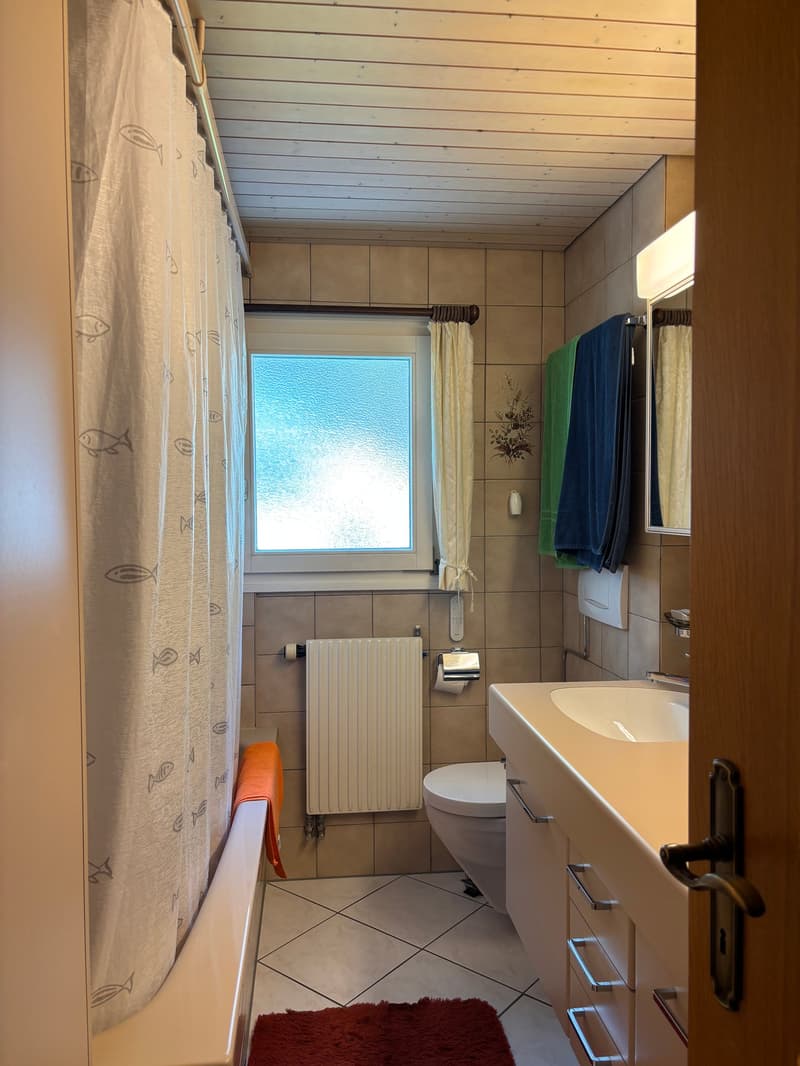Bathroom with bathtub, toilet, sink, mirror, towel rack, radiator, window, and tiled floor.