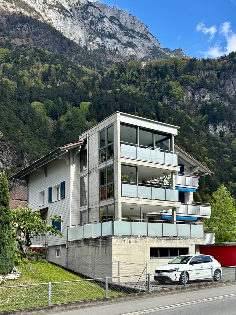 Modern white house with multiple balconies, concrete ground floor, mountain view