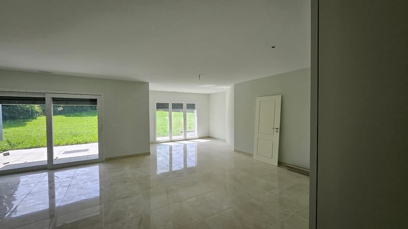 A large room with sliding doors leading to a balcony and a garden view