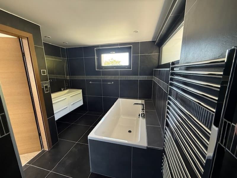 Bathroom with black tiles, white bathtub, white sink, wooden door, window, towel rack