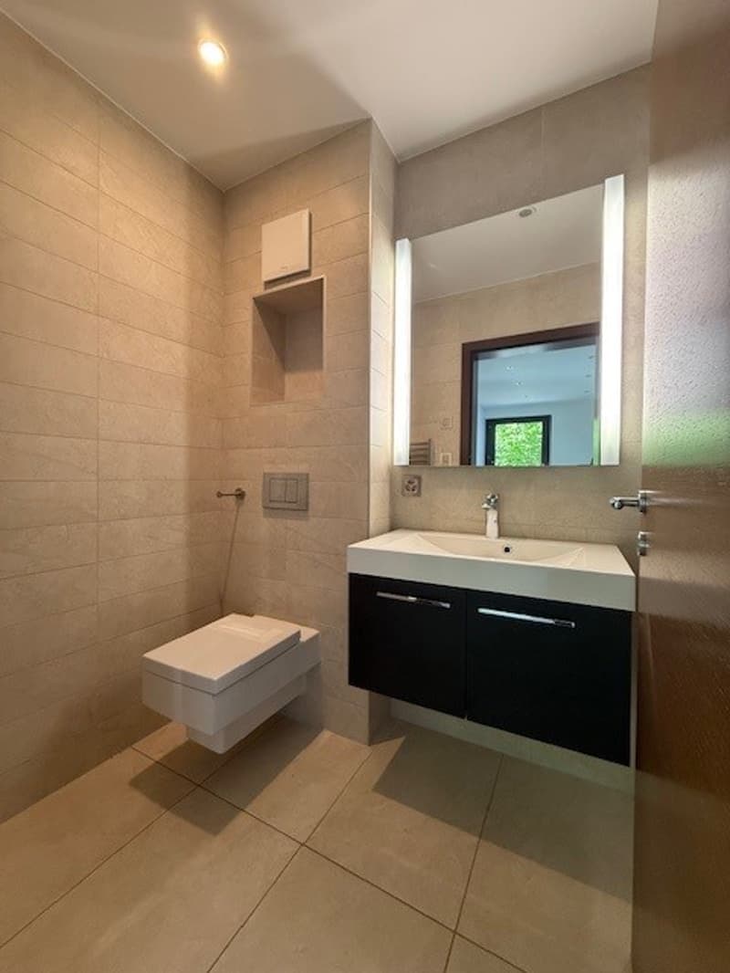 Bathroom with white toilet, sink, mirror, and tiled walls and floor.