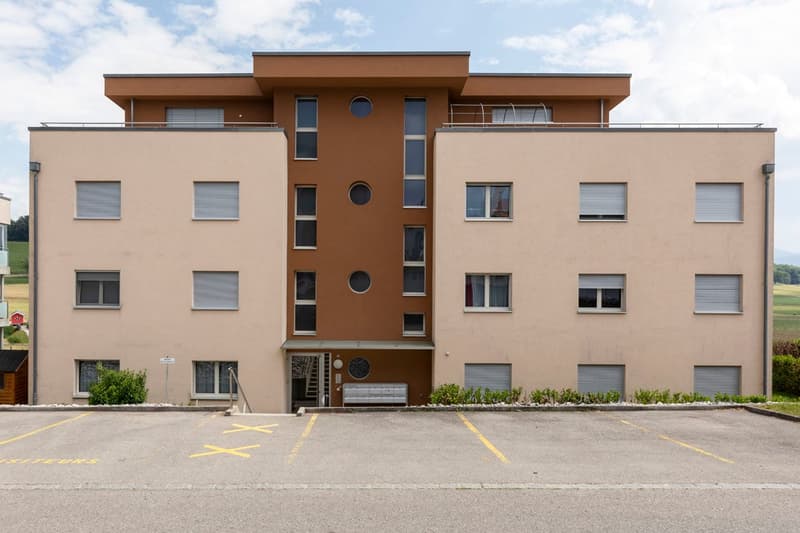 Multi-story apartment building, beige wall, windows with shutters, parking lot