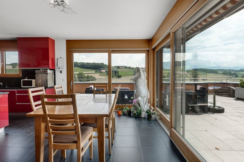 Dining room with wooden table and chairs, large windows leading to a terrace, red kitchen cabinets, wooden ceiling
