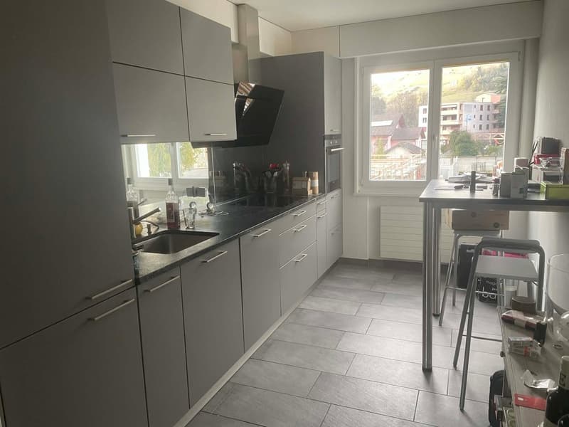 modern kitchen with gray cabinets, black countertops, stainless steel sink, oven, and refrigerator, large window with view