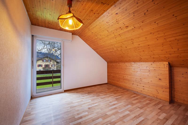 Attic room with wooden ceiling and walls, hardwood floor, large window with view of outdoor scenery