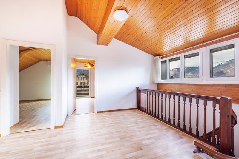 Spacious room with wooden ceiling and walls, hardwood flooring, large windows offering a scenic mountain view, and a wooden railing along the upper level.