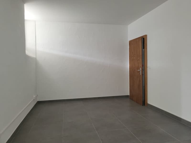 Empty room with white walls, gray tile flooring, and a wooden door.