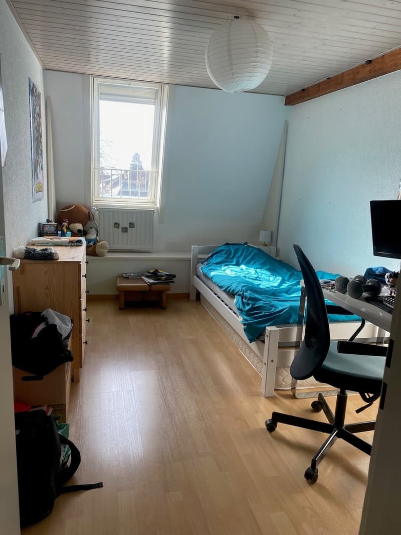 bedroom with bed, desk, chair, wooden floor, white walls, window, wooden cabinet, toys, lamp, backpack