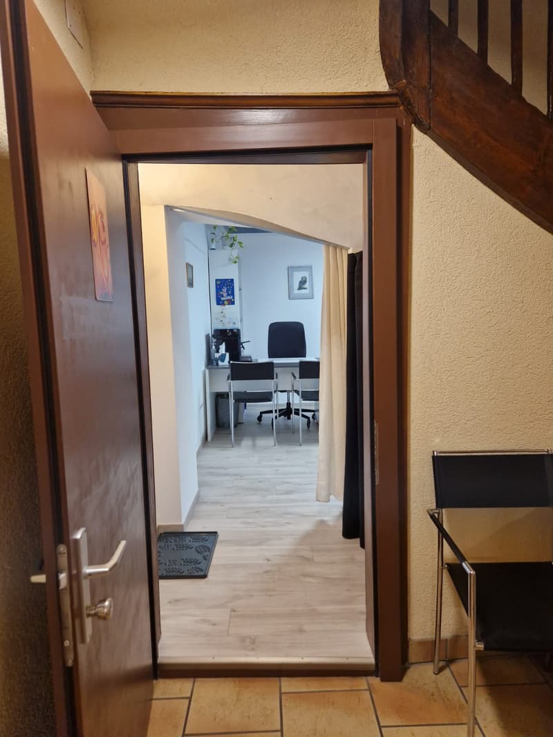 Open door leading to a room with wooden floor, desk, chairs, and a staircase