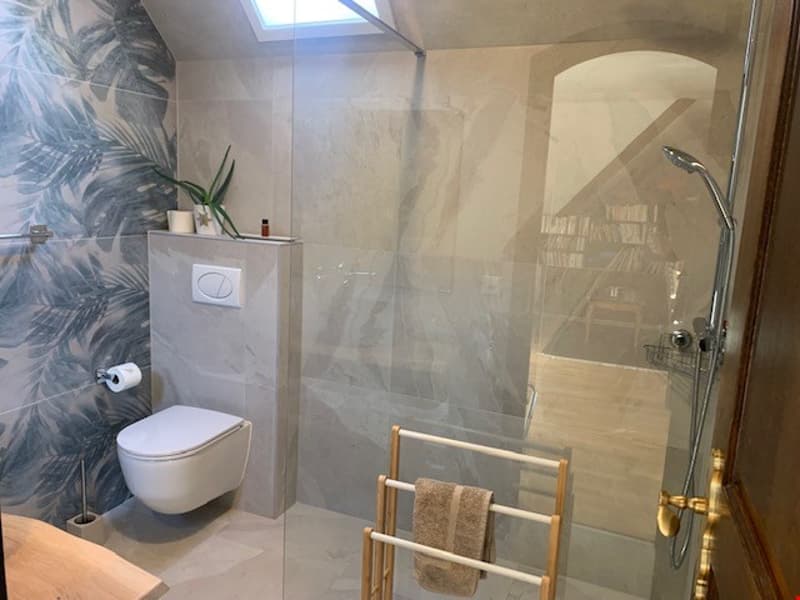 Spacious bathroom with a glass shower enclosure, toilet, and a towel rack. The walls feature a tropical leaf pattern, creating a relaxing and spa-like atmosphere.