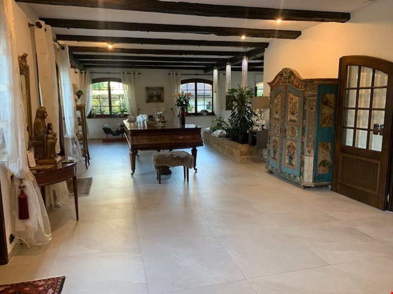 Large open-concept living space with hardwood floors, exposed wooden beams, and a fireplace. The room features a grand piano, antique furniture, and decorative elements like a carved wooden screen.