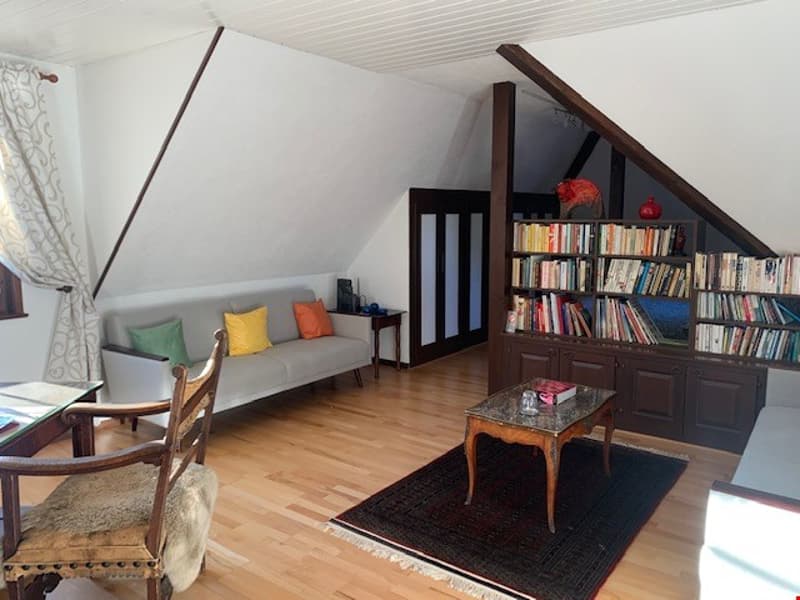 Cozy attic living room with slanted ceilings, hardwood floors, built-in bookshelves, sofa, and coffee table