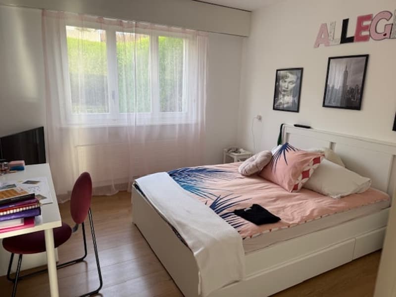 A bedroom with a bed, desk, and window with curtains.