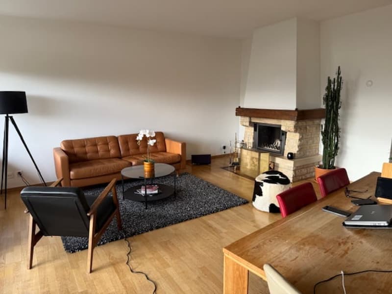 Fireplace, wooden floor, brown leather couch, round coffee table, standing lamp, dining table with laptop, black chair, armchair, ottoman