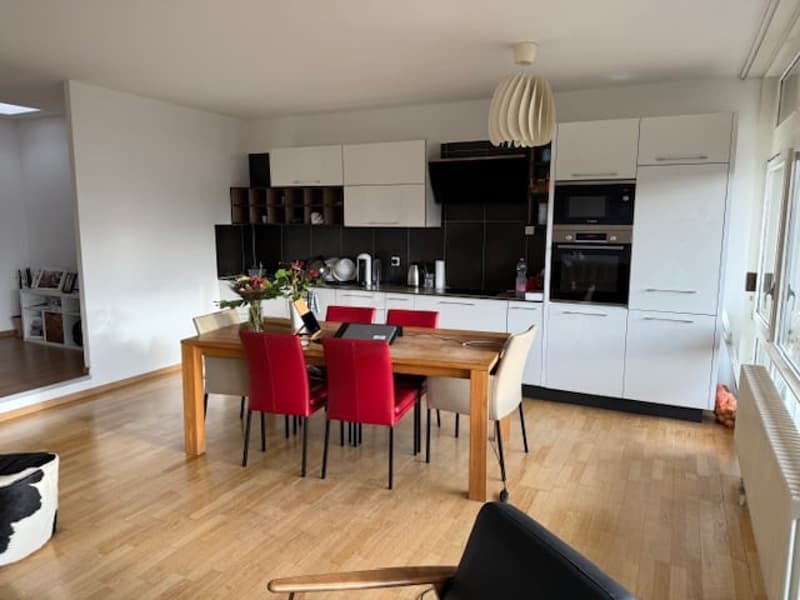 Dining room with wooden floor, wooden table, red chairs, white cabinets, black counter, oven, microwave, radiator, flower vase, pictures