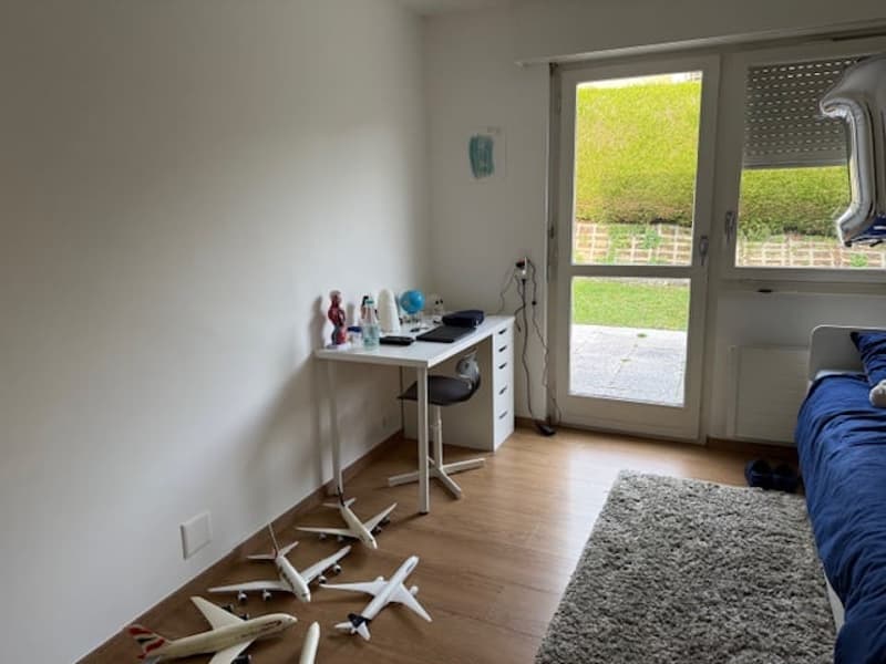 A room with a desk, chair, bed, wooden floor, and white walls