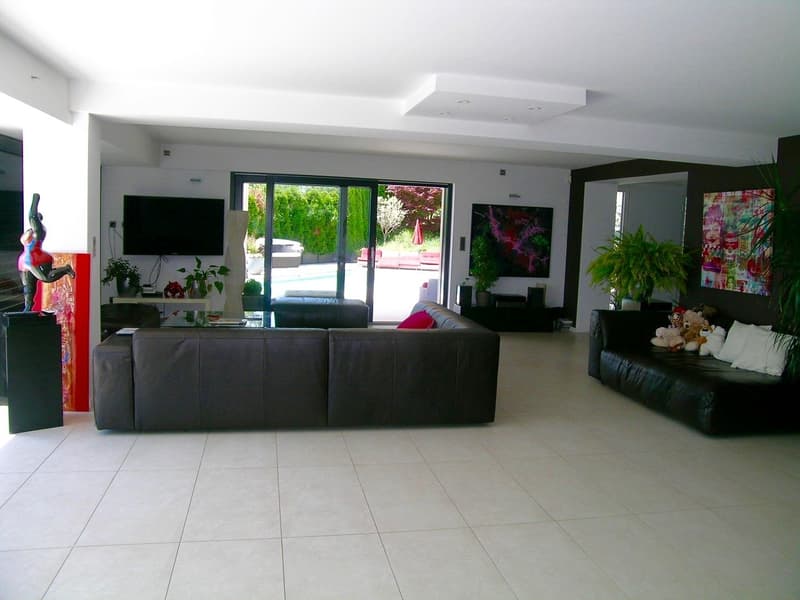 large living room, two sofas, coffee table, TV, plants, sliding glass doors, pool view