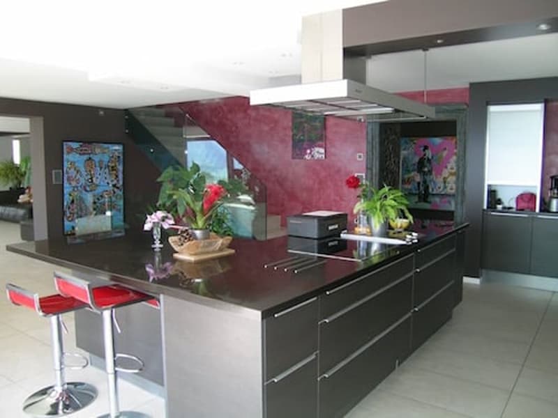 modern kitchen with island, red walls, black countertops, stainless steel appliances, red stools, plants, artwork