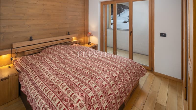wooden walls, wooden floor, bed with red and white bedspread, nightstands with lamps, sliding glass doors with balcony view
