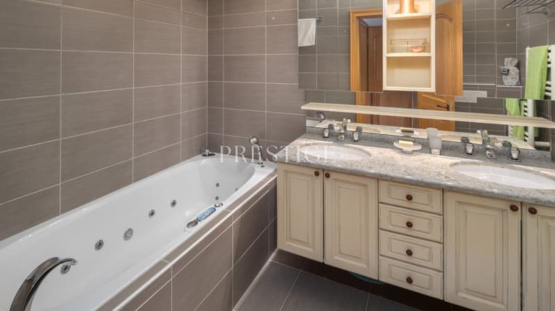 Bathroom with bathtub, double sink, mirror, wooden cabinets, towel rack, and towel