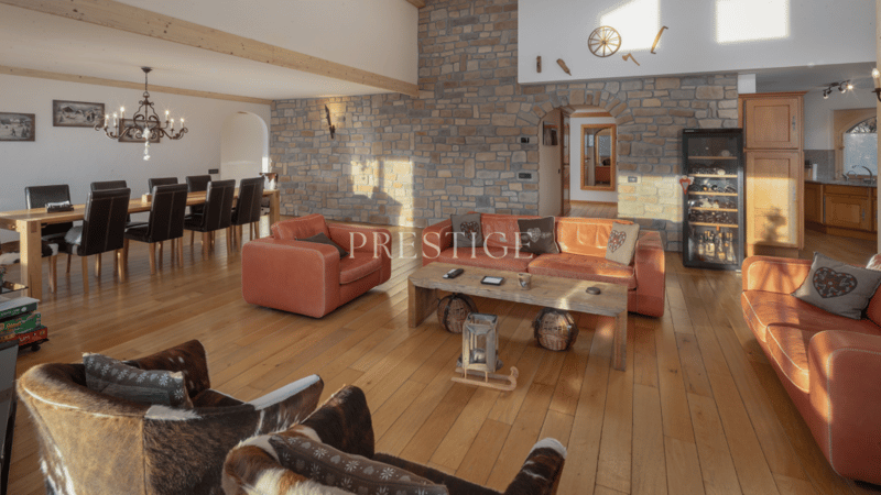 Large room with wooden floor, stone wall, dining table with chairs, fireplace, leather couches, wooden coffee table, chandelier