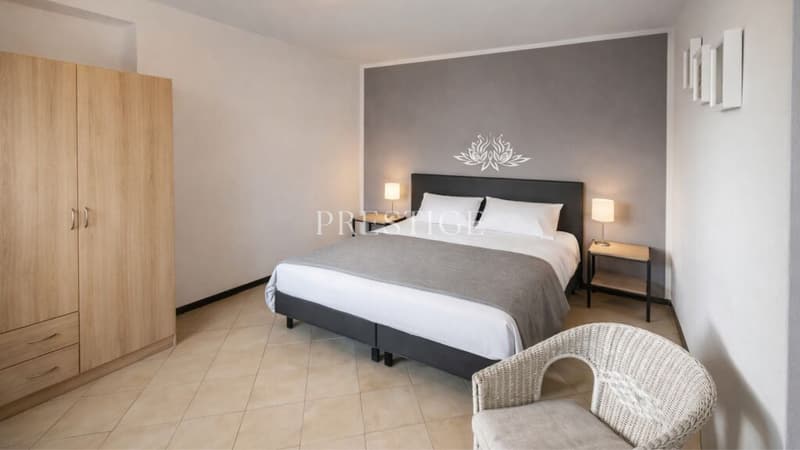 single bed, nightstands, lamps, wicker chair, wooden wardrobe, grey walls, beige flooring