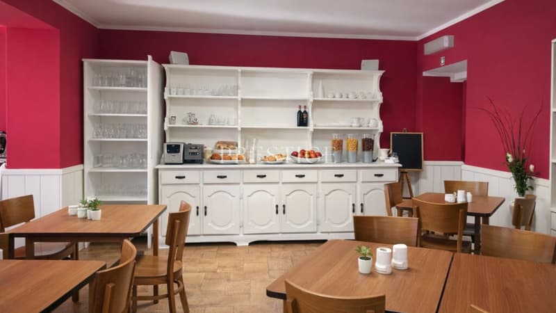 Dining area with a buffet, red walls, wooden tables and chairs, wooden floors, open shelves with glasses and dishes