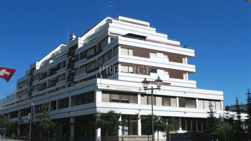 Modern, multi-story building, white with brown accents, large glass windows, red flag