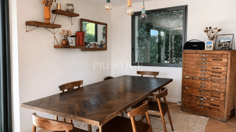Wooden dining table, four wooden chairs, white walls, large window, wooden cupboard, mirror, shelf with decor items