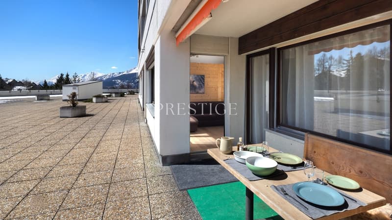 Outdoor dining area with wooden table, green plates, glasses, and a view of the mountains