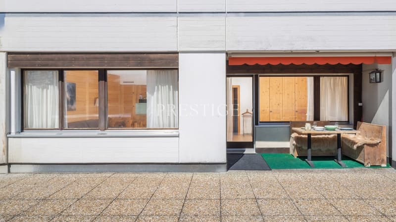 white exterior, large windows, wooden door, balcony with table and chairs, green rug