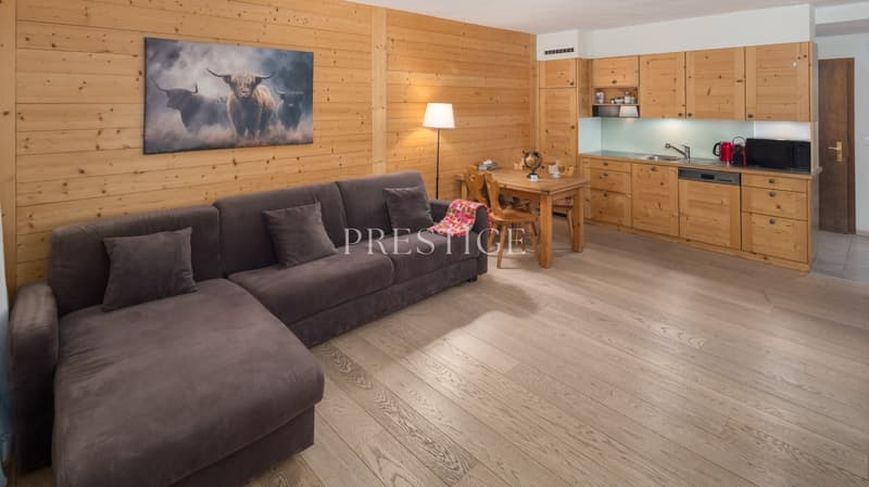 living room with wooden floor, wooden wall, sofa, wooden table, wooden chairs, lamp, kitchen with wooden cabinets, sink, dishwasher, microwave, refrigerator