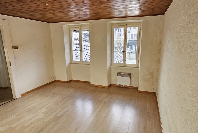 empty room with wooden floor, white walls, windows with a view of other buildings