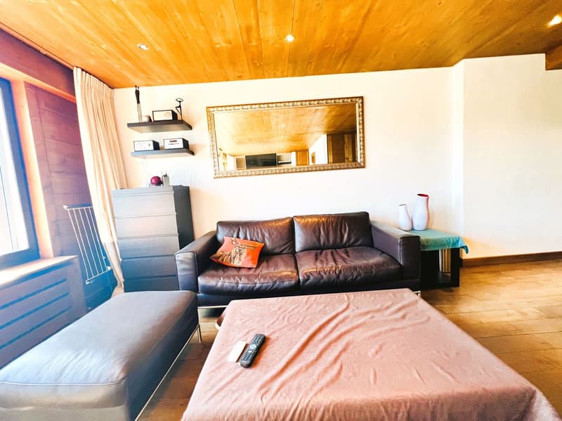 Cozy living room with wooden ceiling, leather sofa, shelves, and a large framed mirror on the wall