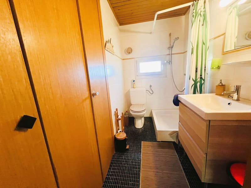 Bathroom with a toilet, bathtub, sink, wooden storage, black tiled floor, wooden bench, mirror and shower attachment