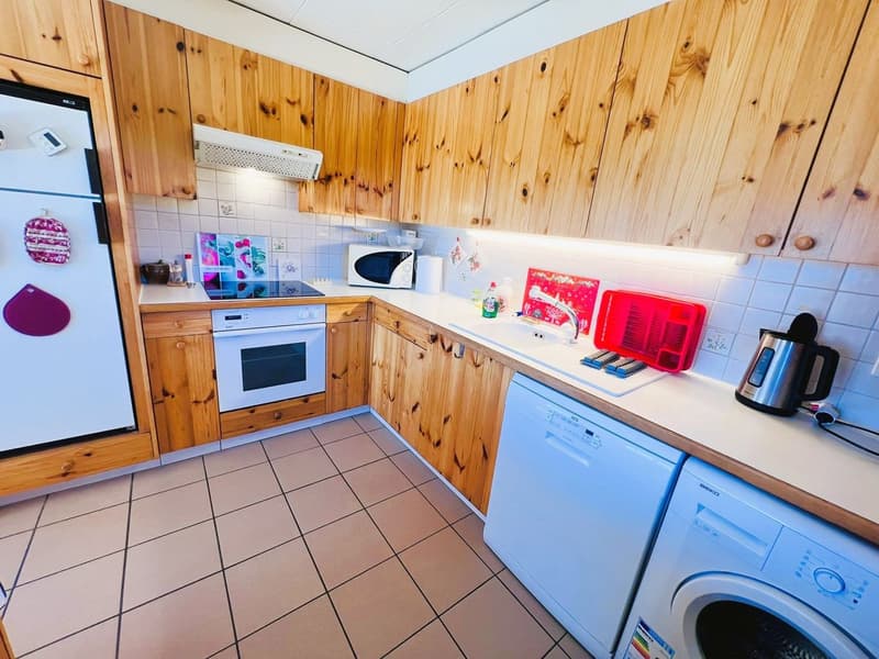 Kitchen with wooden cabinets, tiled floor, fridge, dishwasher, oven, microwave, sink, countertop, coffee maker, and several kitchen appliances.