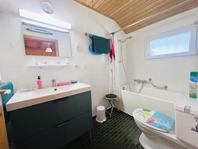 tiled walls and floors, white sink, black cabinet, bathtub, toilet, shower, window