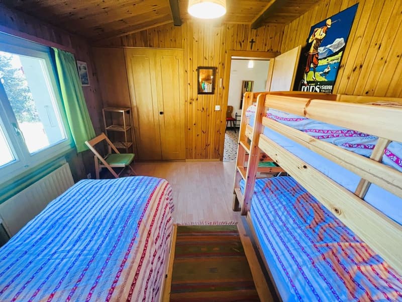 Single bed, bunk beds, small shelf, radiator, rug, wooden walls, large window, open door