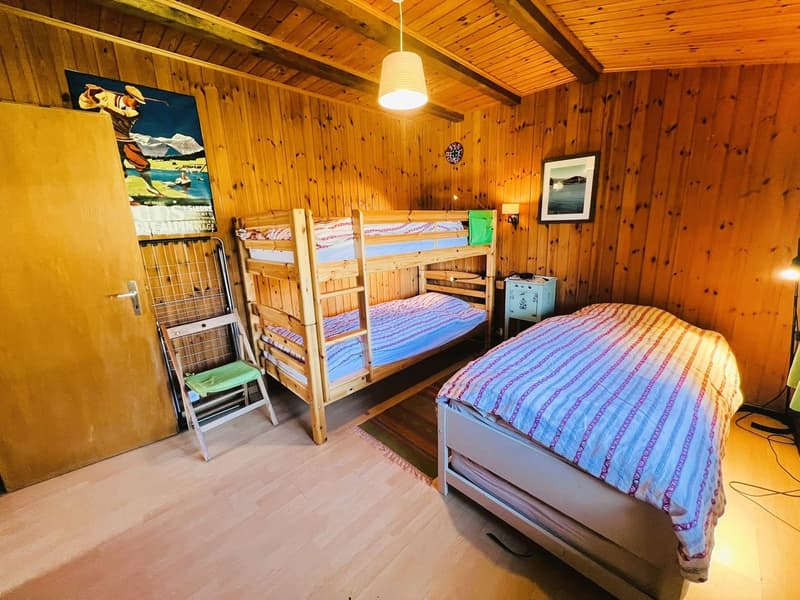 Wooden bedroom with bunk beds, a single bed, chair, desk, paintings, wooden floor, wooden ceiling
