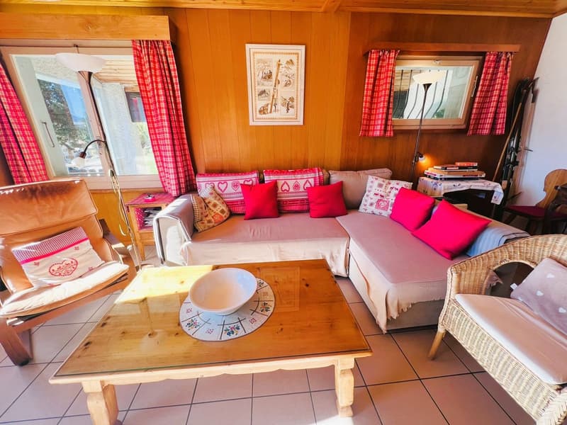 L-shaped sofa, decorative cushions, wooden coffee table, wooden floor, wooden armchairs, lamps, picture frame, red curtains, windows, books, table with books and magazines