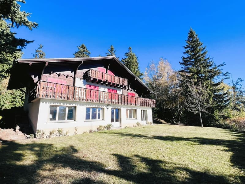 2 story chalet house, white exterior with red shutters, wooden balcony with railing, green lawn, trees surrounding