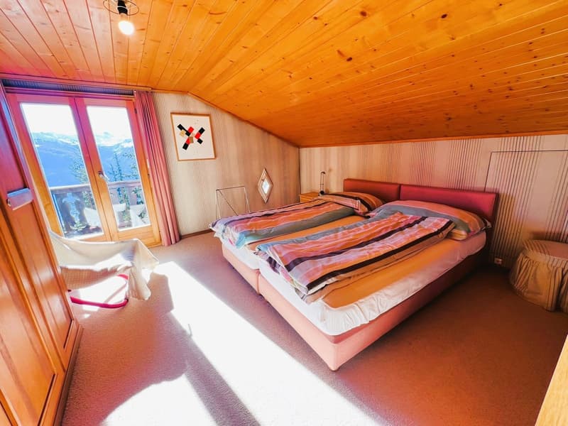 a bedroom with a balcony, double beds, nightstands, bedside lamps, chair, picture frames, and a wooden ceiling